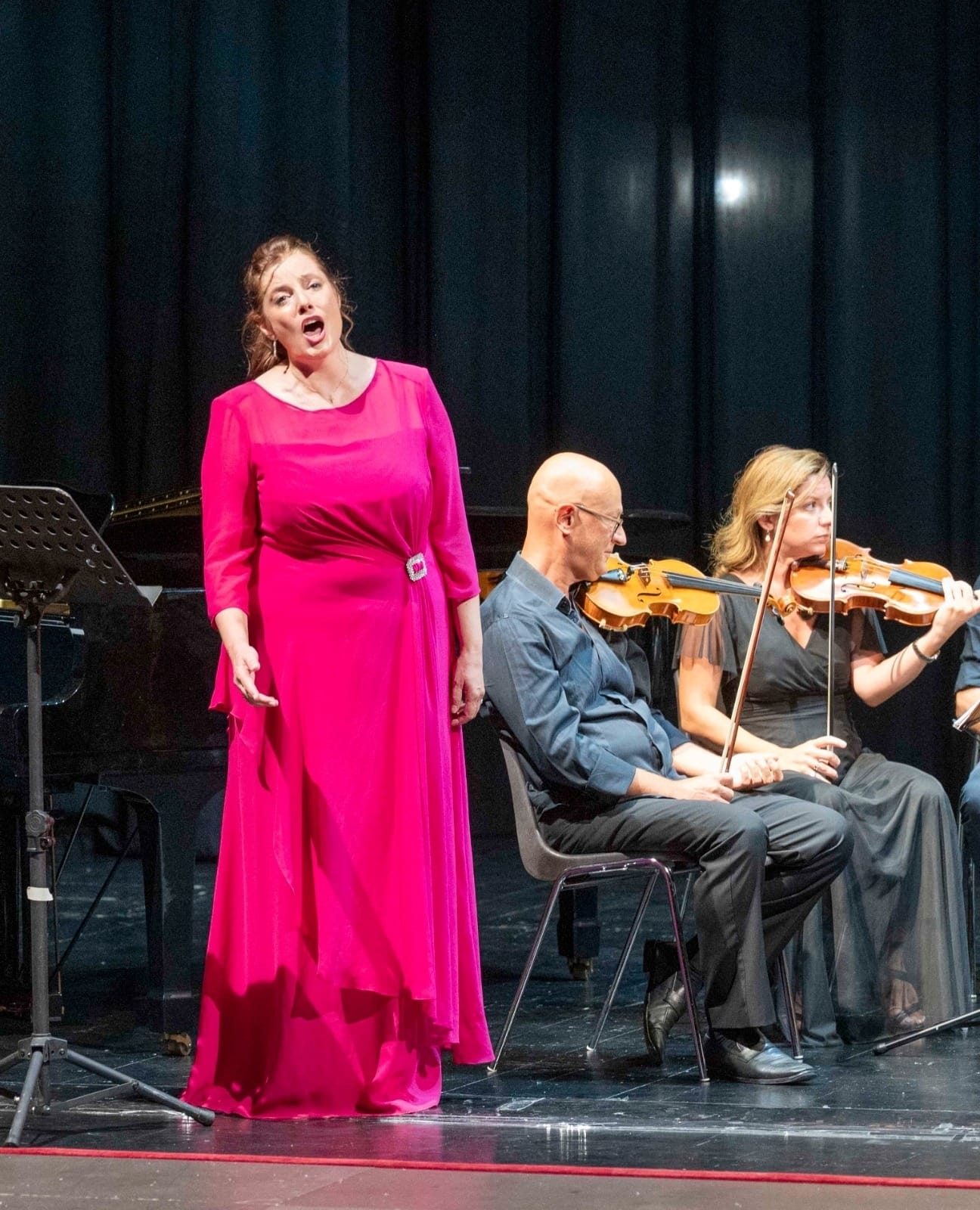Vanessa Ayllón, con vestido fucsia, canta en concierto junto a dos músicos de cuerda ante un telón negro