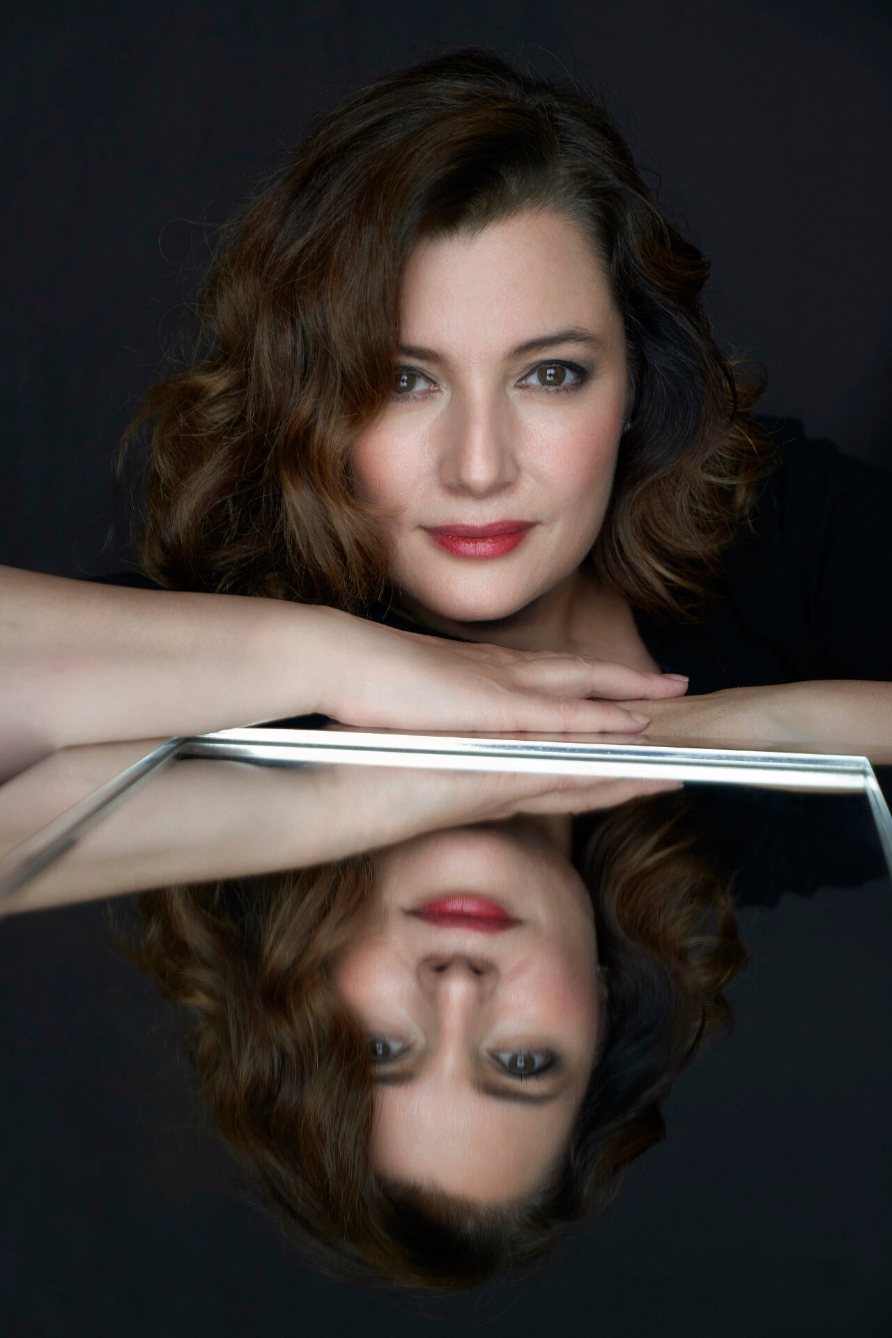 Retrato de Vanessa Ayllón junto a un espejo que refleja su rostro, sobre fondo oscuro